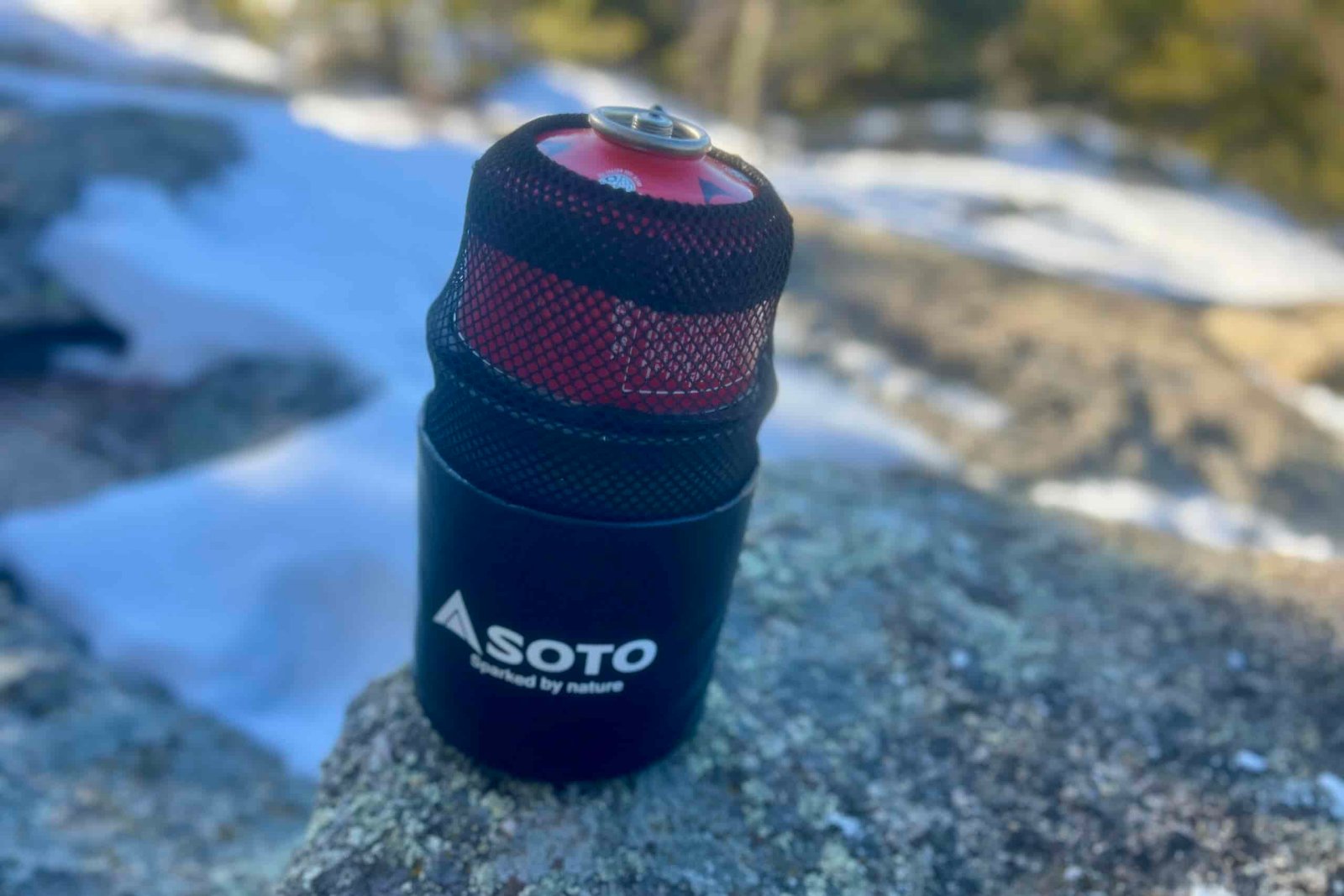 The soto thermostack combo sits packed together on a rock with a fuel canister cinched in the mesh stuff sack.