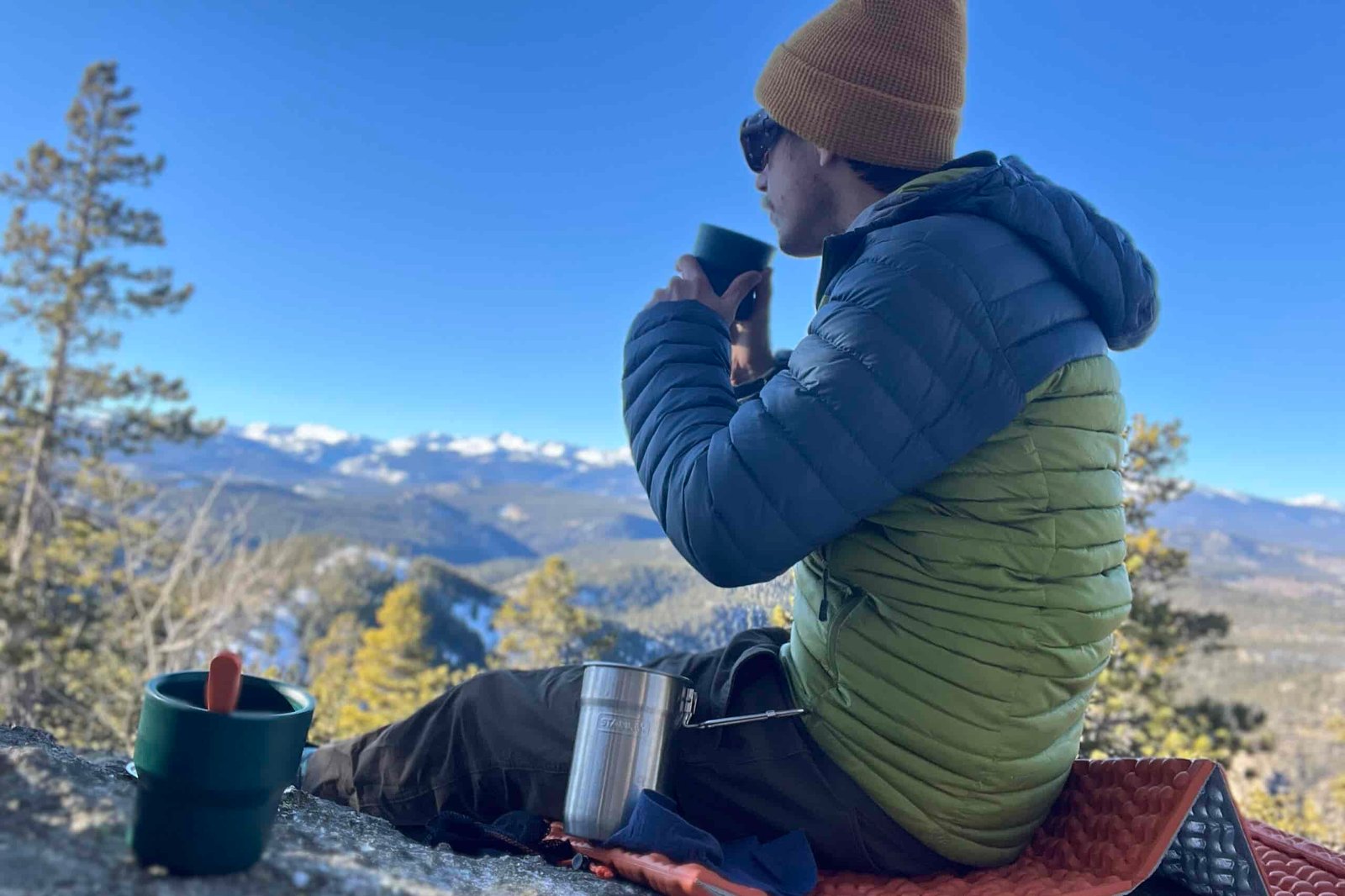a backpacker drinking from his stanley nesting cup on a cold and sunny morning