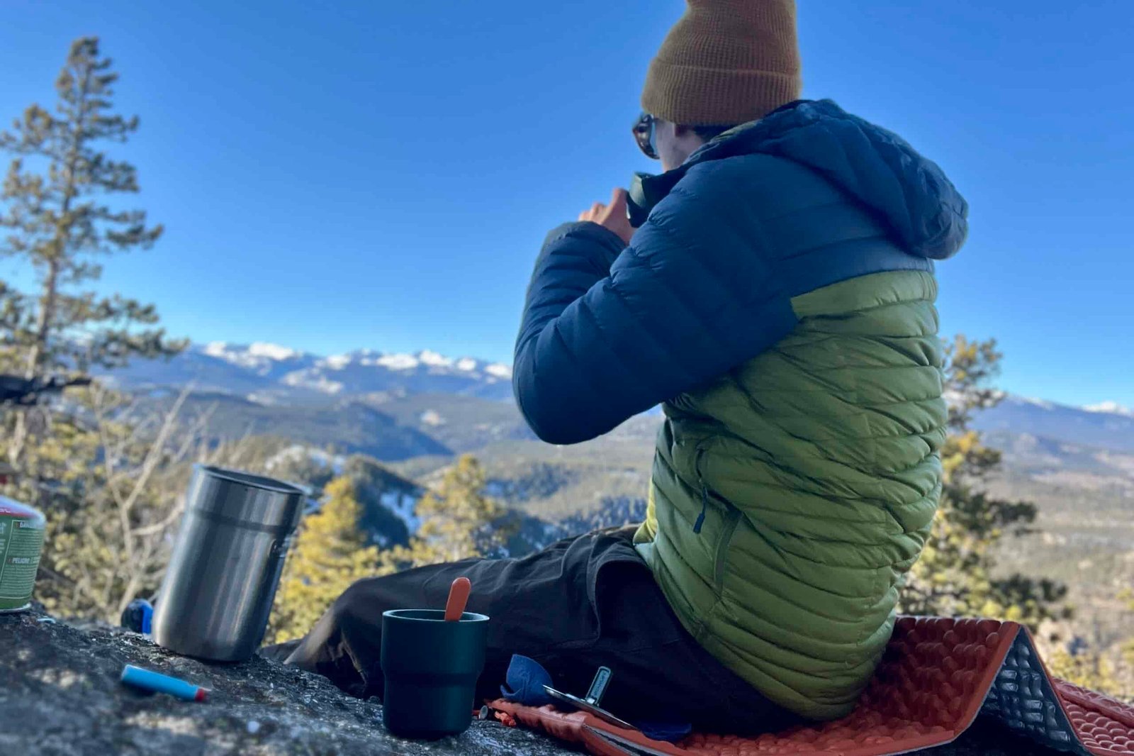 man drinking coffee in the morning with a nesting cup made by stanley while sitting on a rock ledge over a valley