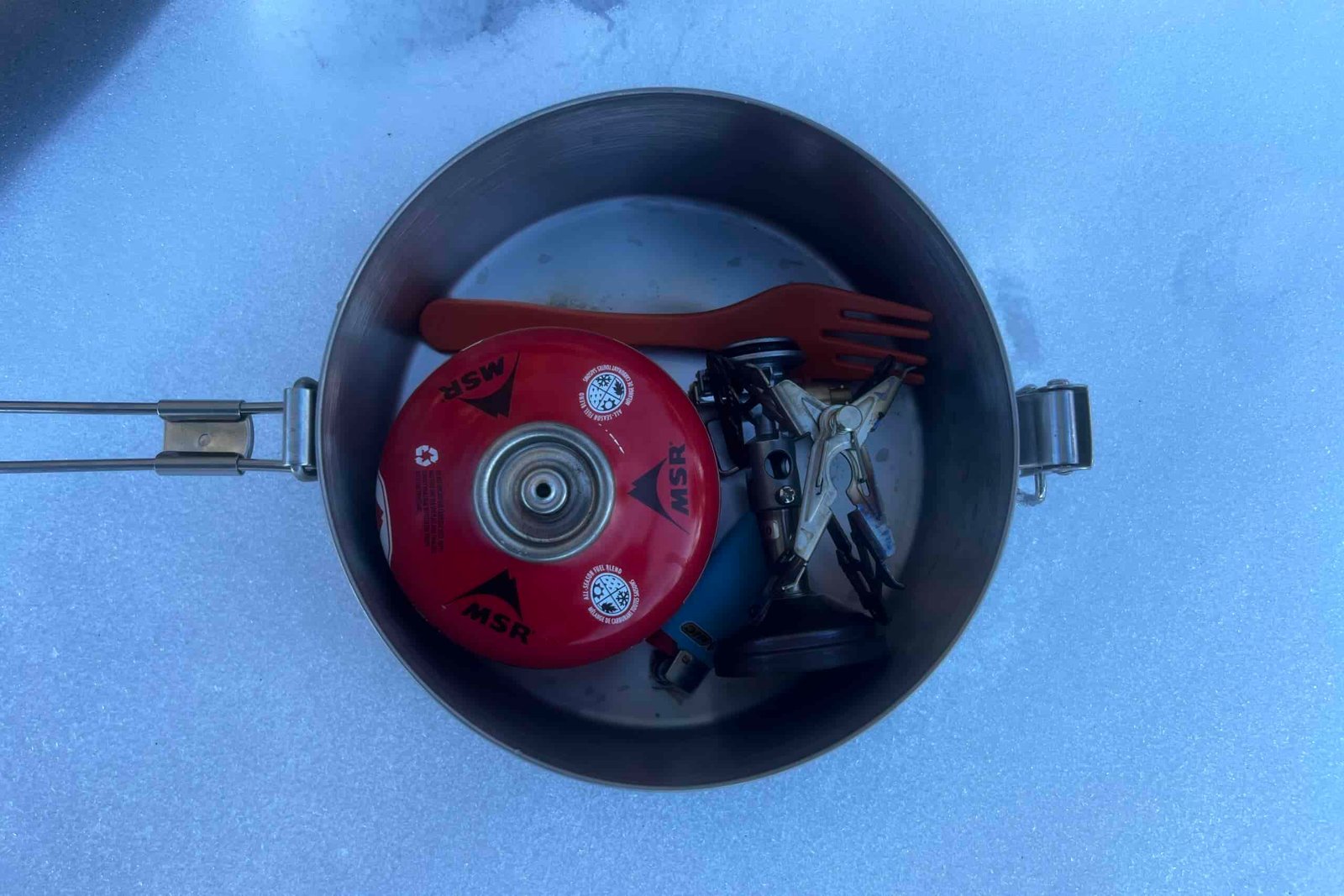 a top down view of fuel, a stove, fork, and lighter packed into a steel pot.