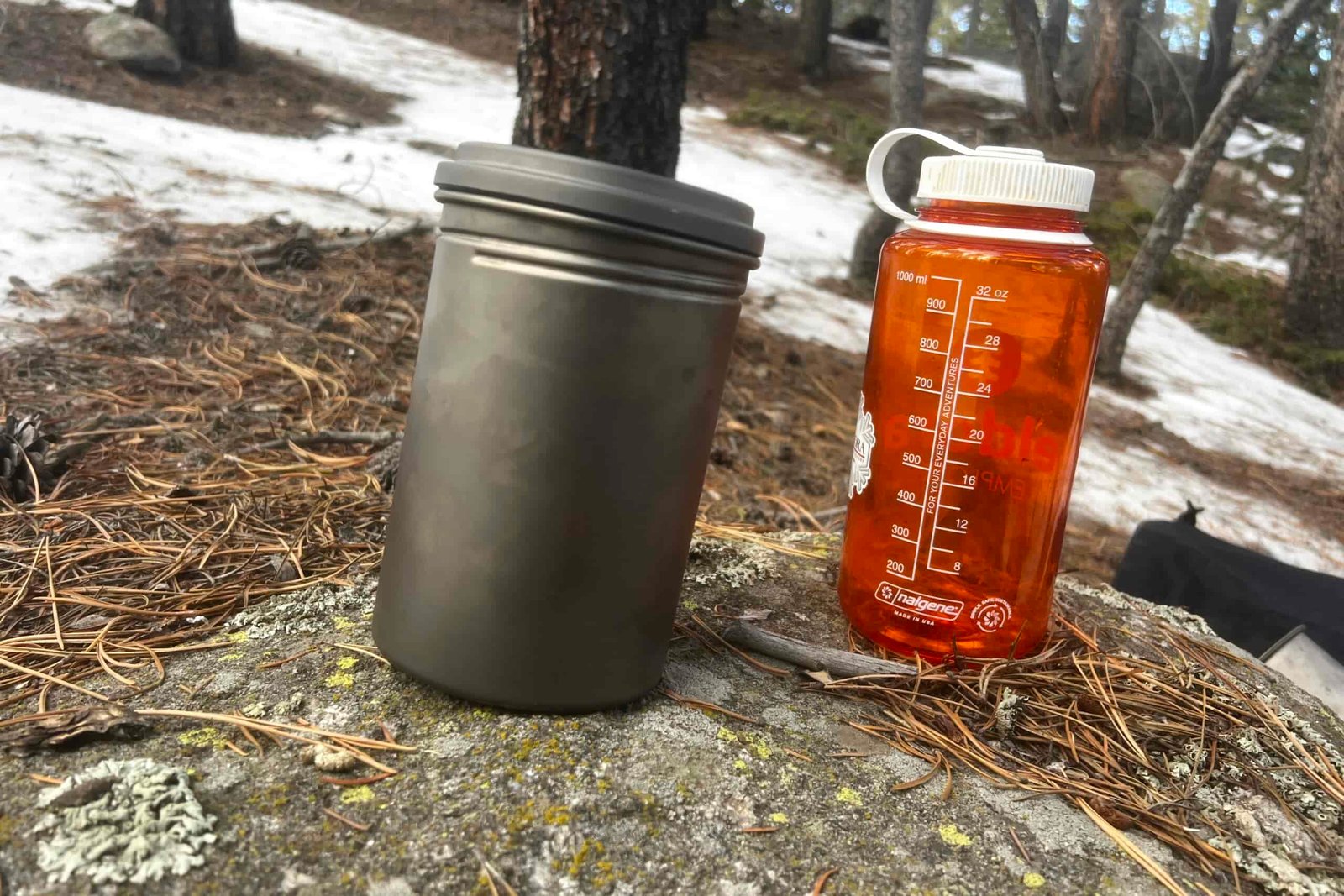 A titanium pot sits next to a nalgene bottle on a rock.