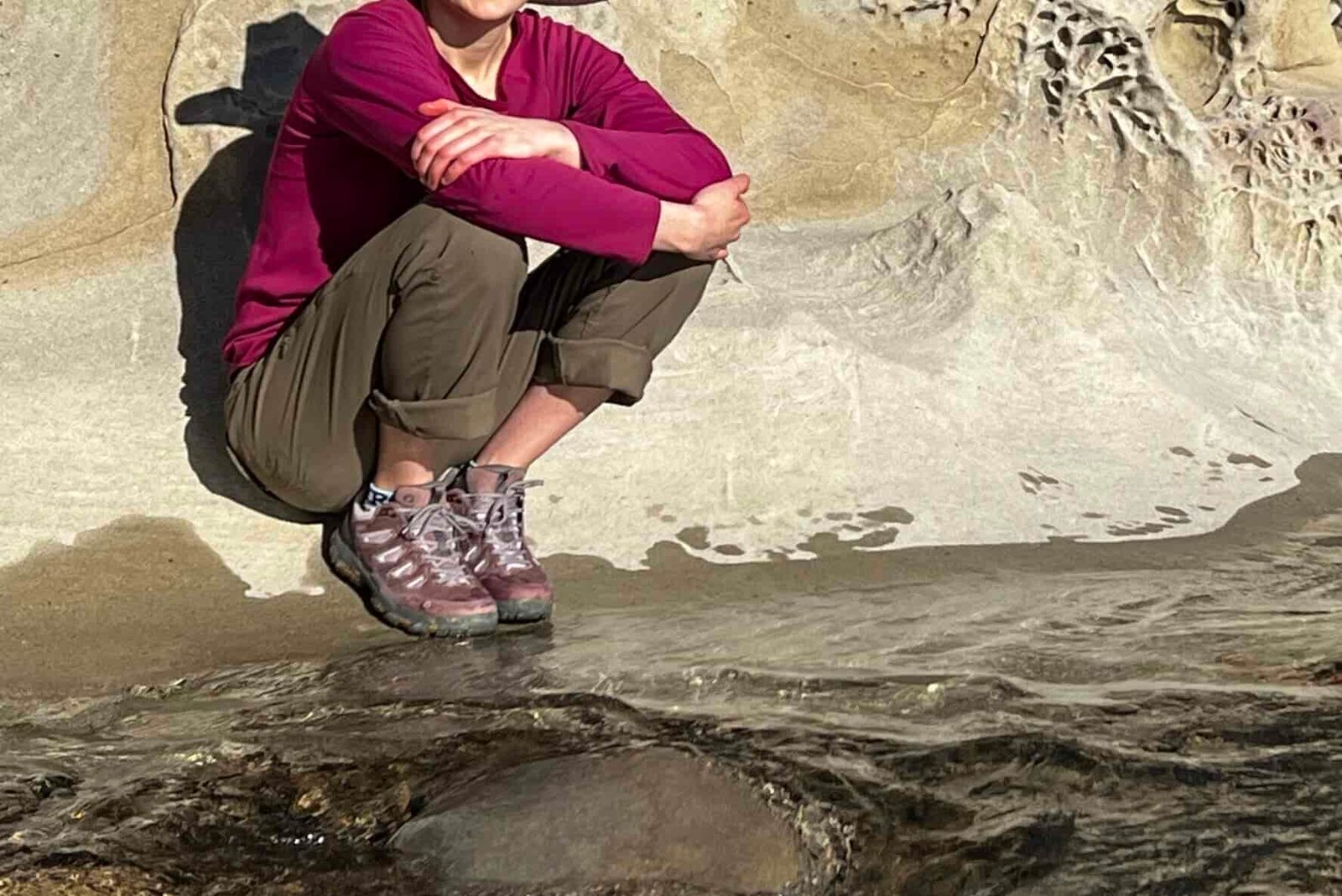 Women squatting next to a creek with a boulder in the background.