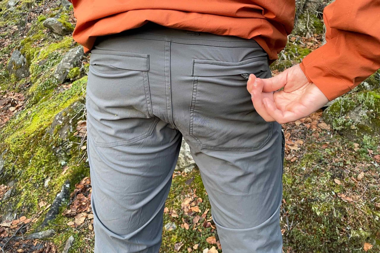A closeup of a man zipping close a rear pocket on a pair of pants.