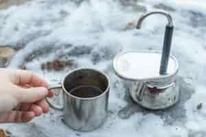A hand grabs the small cup full of coffee from next to the GSI Mini Espresso.