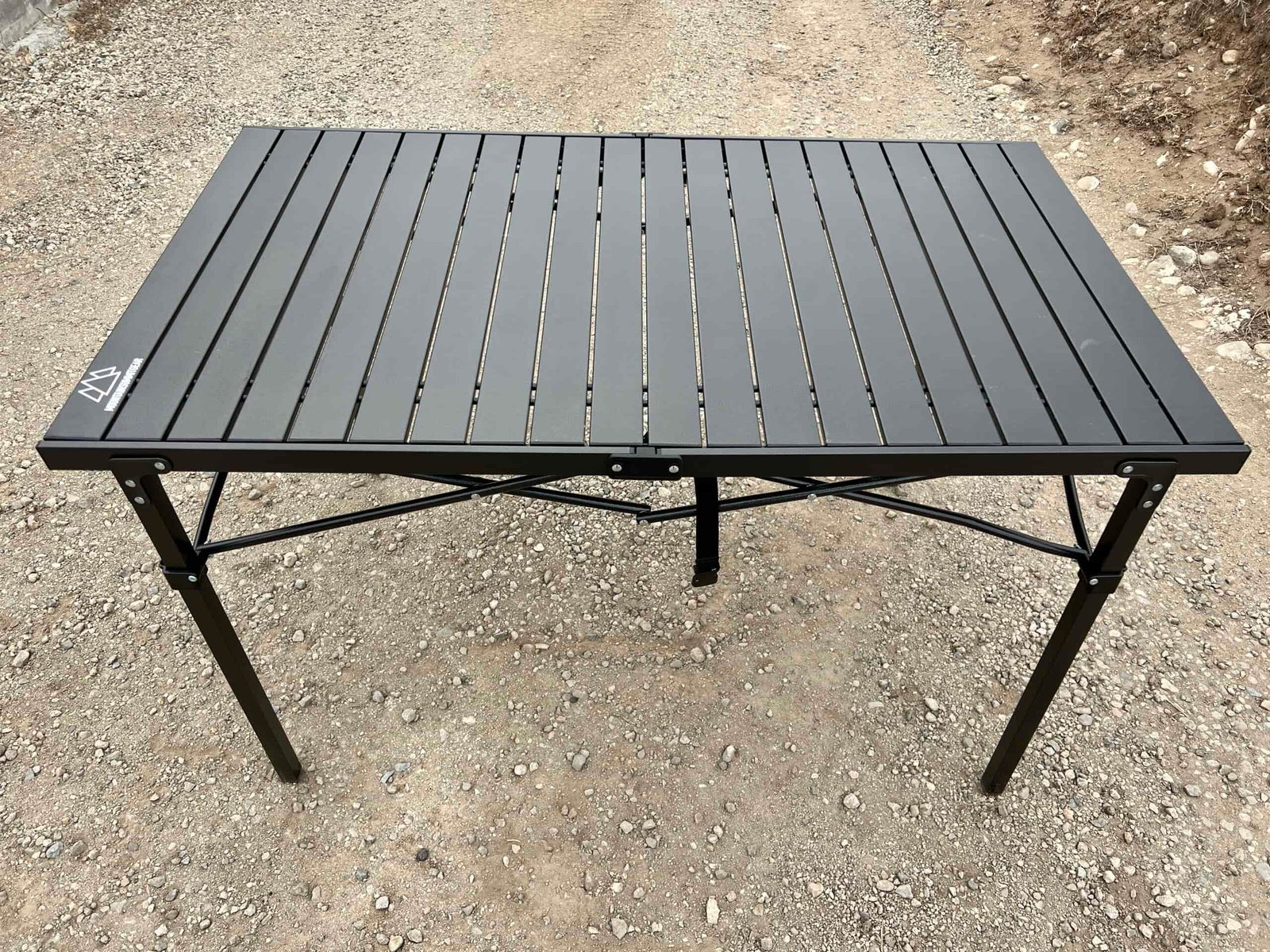 The Mountain Summit Gear Heavy Duty Roll Top Table stands on gravel.
