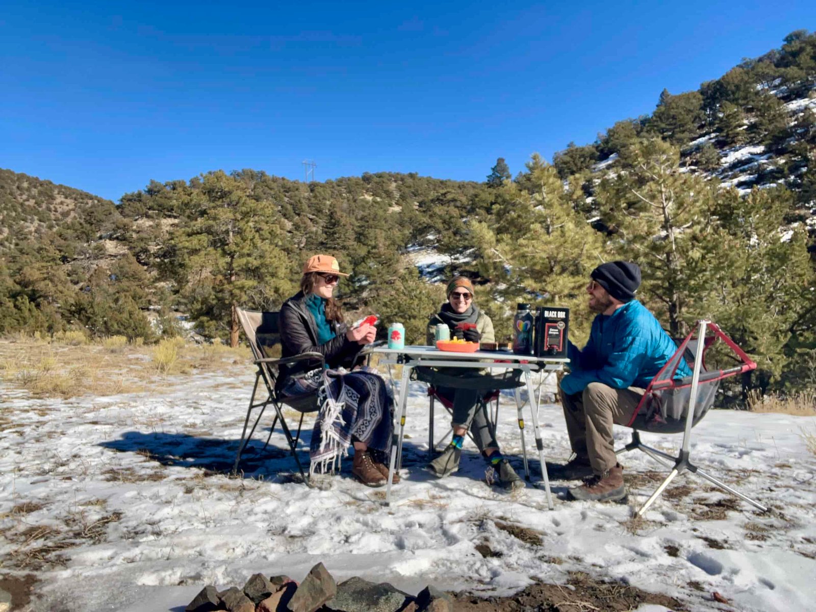 Three people sit around the Portal Roll-Up Table smiling and holding cards. The background is tree-covered hills and there is snow on the ground.