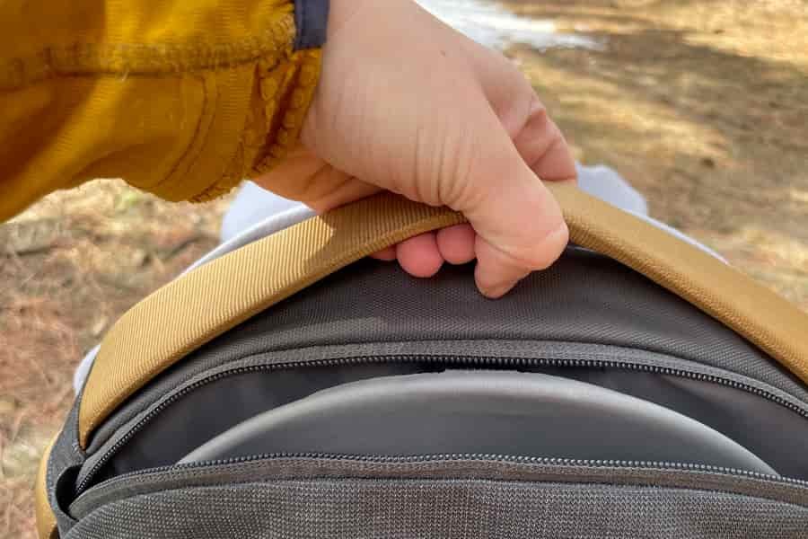 Close-up of a hand holding the padded top handle of the Kelty PerfectFIT Journey Elite carrier, demonstrating its ergonomic design.