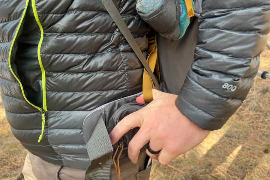 Hand accessing the zippered side pocket of the Kelty PerfectFIT Journey Elite carrier.