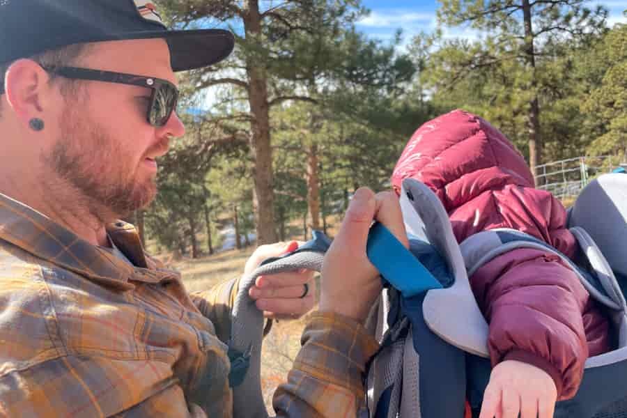 Close-up of a parent adjusting the shoulder straps of the baby carrier for a secure fit.