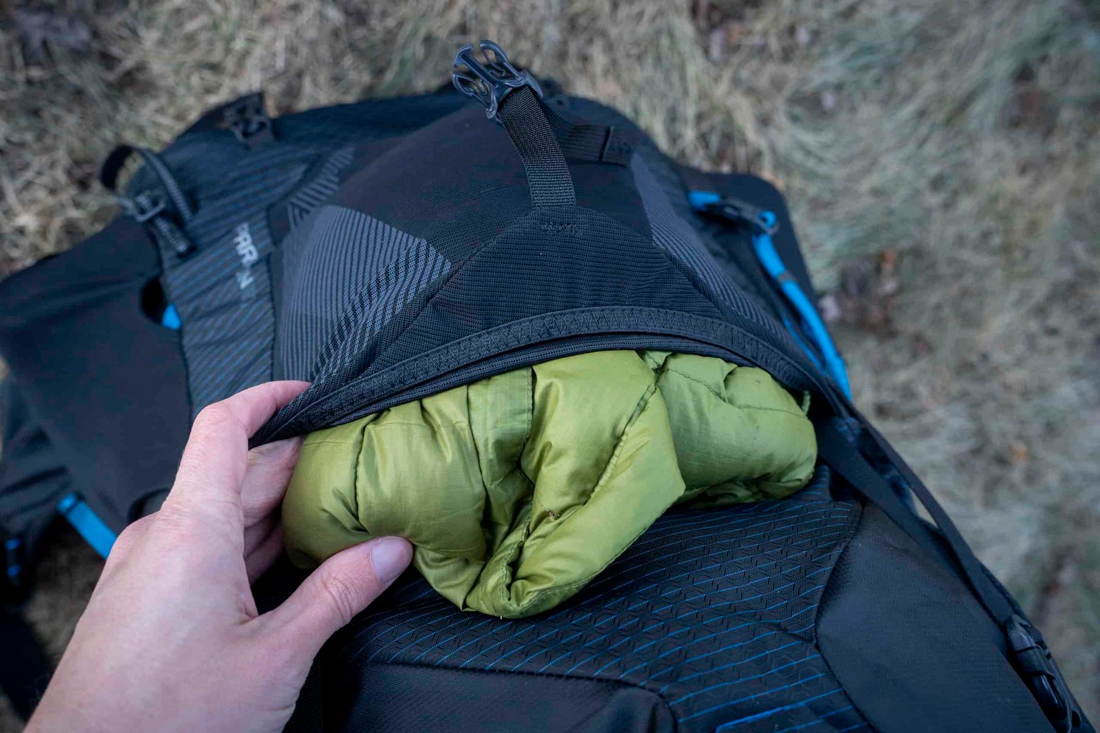 a hand holds a front mesh pockets on a backpack full of a green jacket