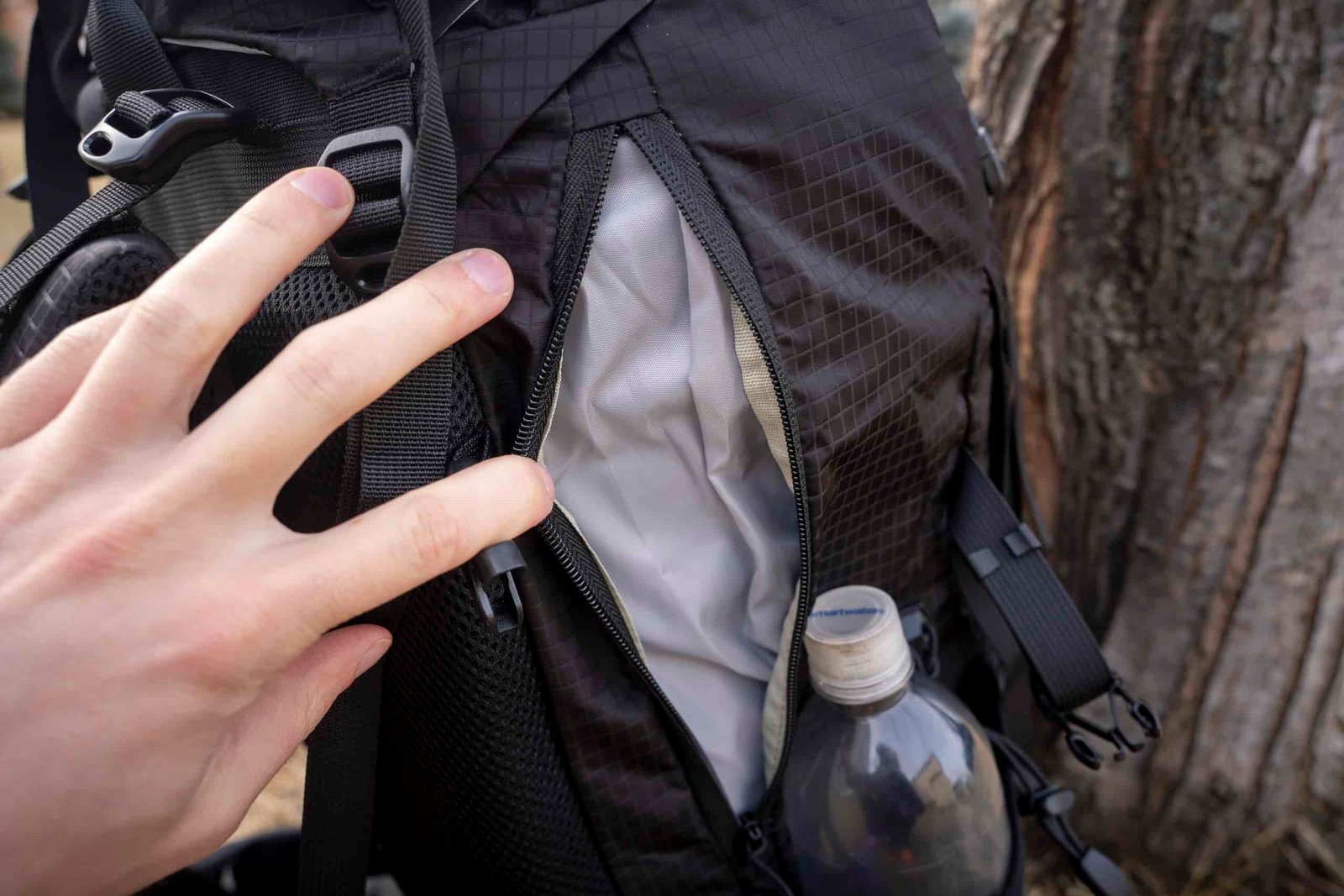 a hand holding open a side pocket zipper on a backpack