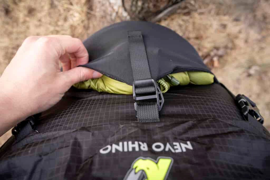 a green jacket is stuffed in a front stretch pocket of a backpck