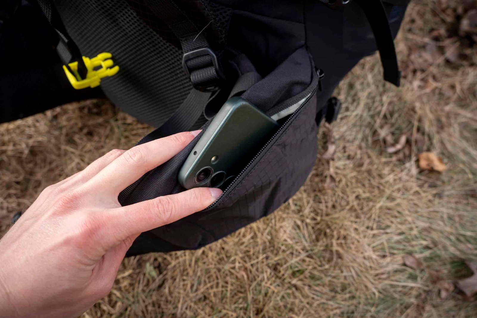 a hand holds a phone in a hipbelt pocket of a backpack
