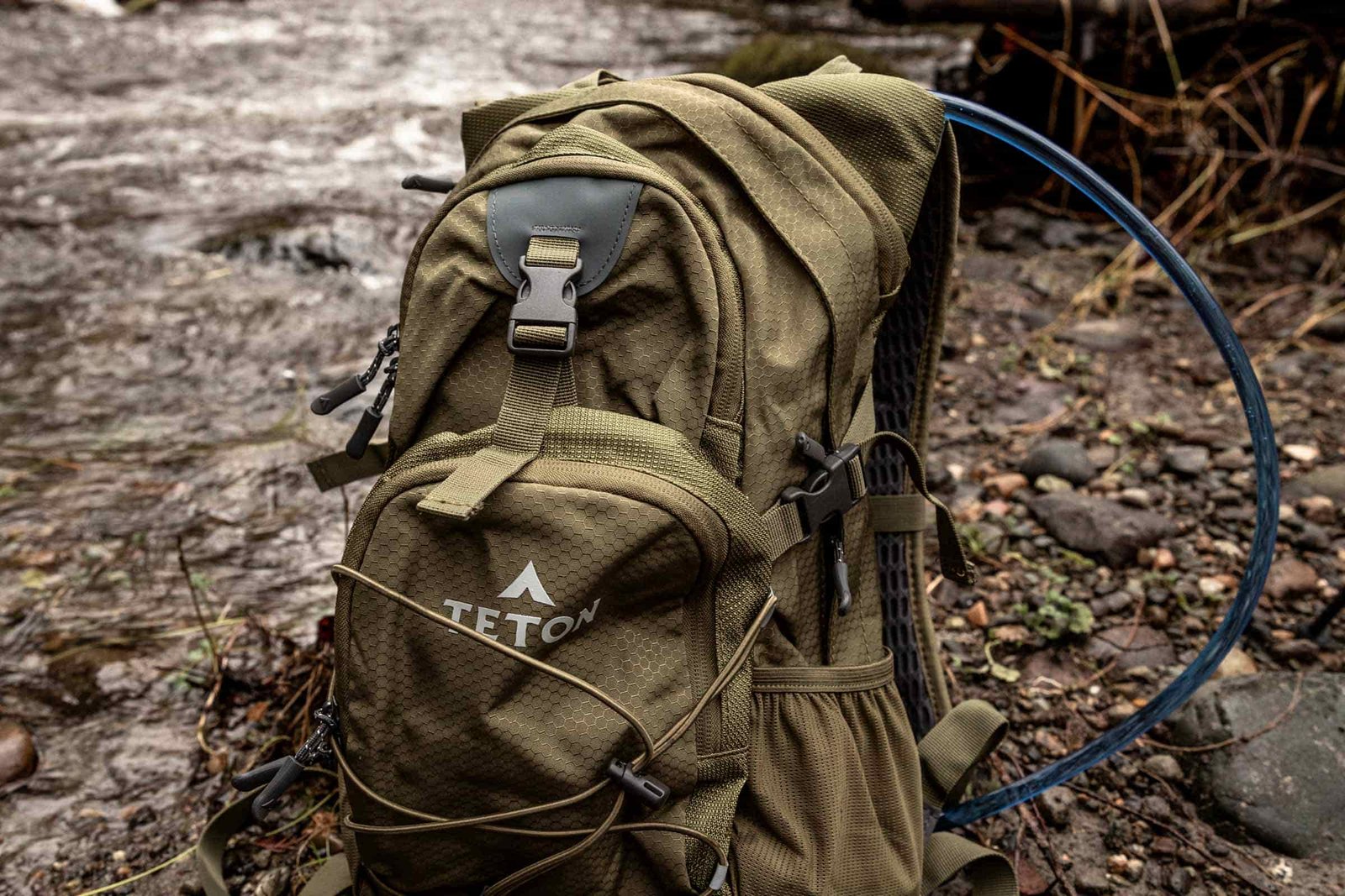 Details of TETON Sports Oasis 18L Hydration Pack - the pack is sitting on the ground by a river