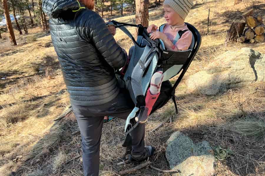 A parent interacting with a child seated in the Thule Sapling, demonstrating the ease of use and adjustability of the carrier.