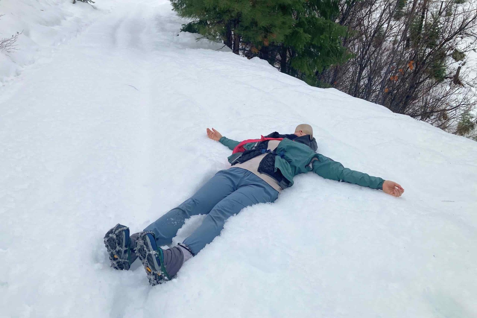 Hiker laying in the snow wearing the Women’s Topo Trailventure 2 WP with gaiters and microspikes on