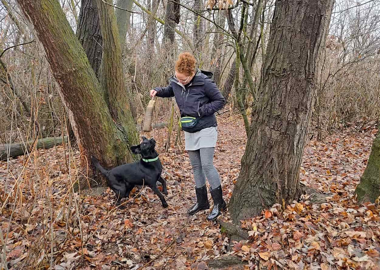 a woman playing with her dog in a forest while wearing a fanny pack by patagonia