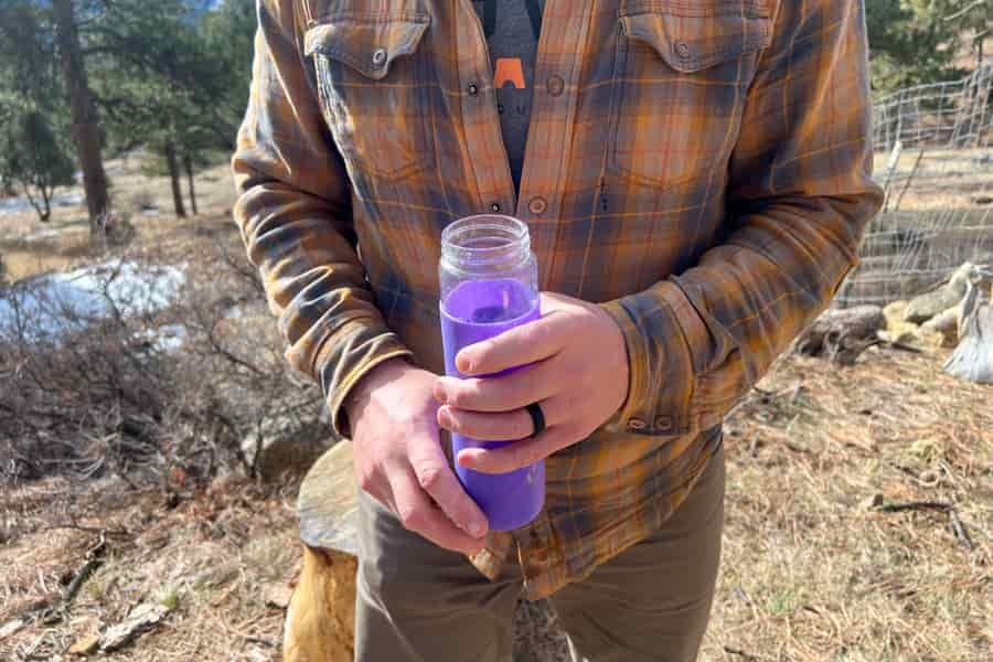 Person holding a purple glass water bottle with both hands in an outdoor setting.