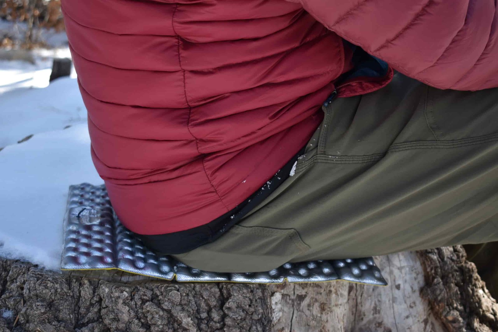Close up of a backpacker siting on a foam pad on a snowy stump