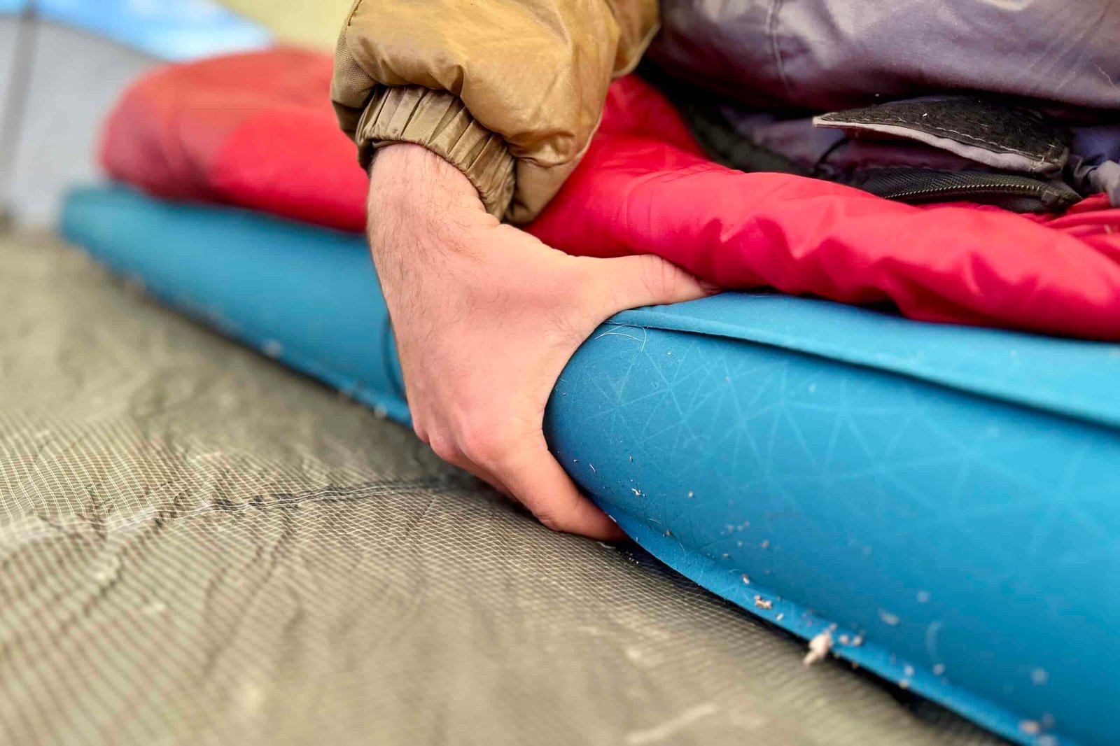 A hand grasps the side of a thick camping mattress.