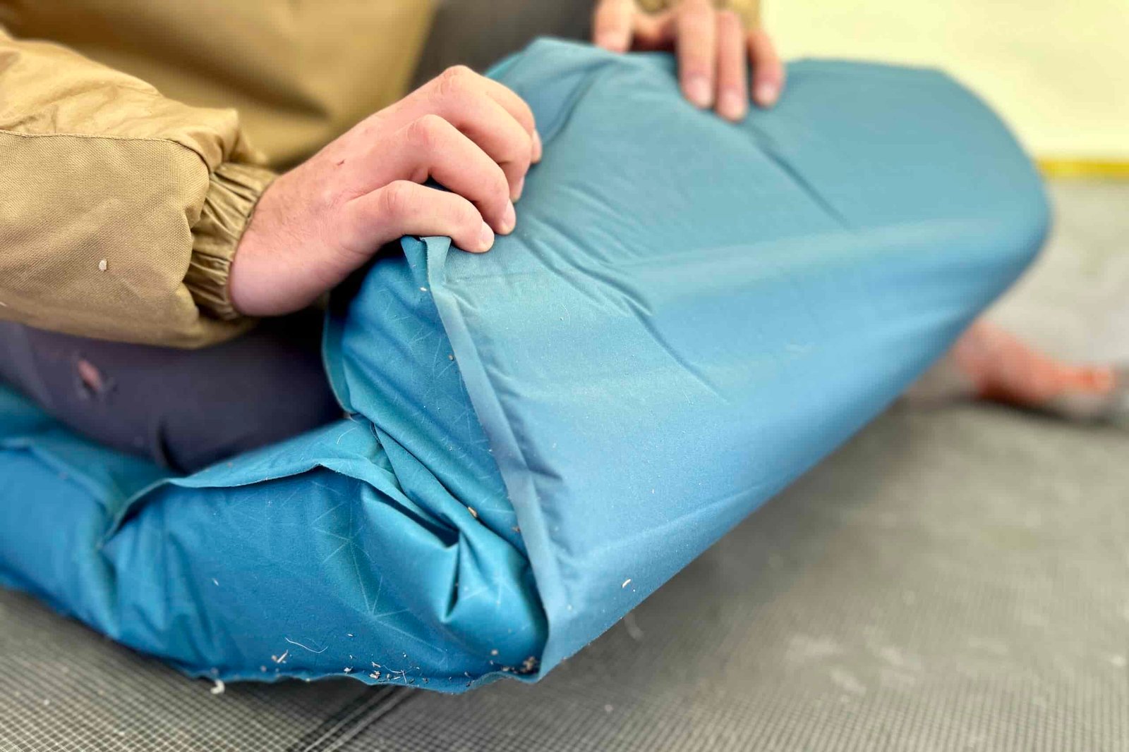 Close-up image of two hands folding the end of a thick camping mattress inside a tent.