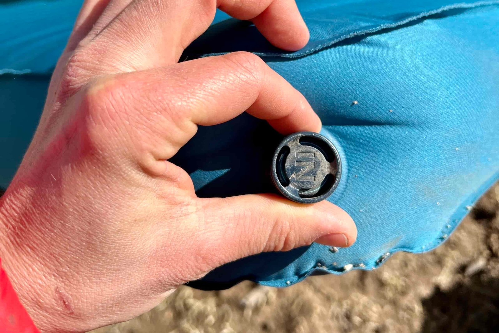 Close-up image of the air intake knob on a sleeping mattress with a person's hand on it, showing how it twists.