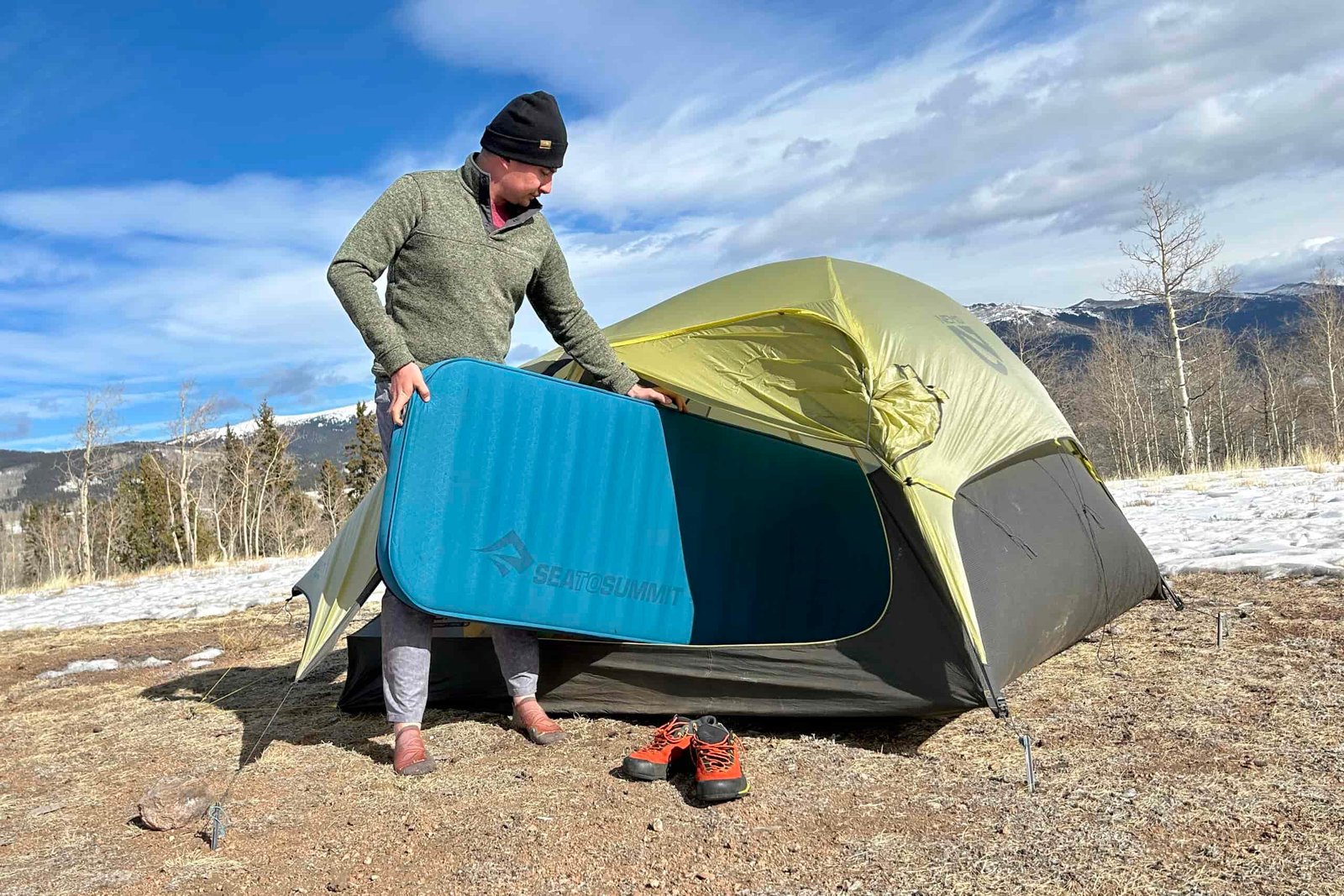 A man loads a camping mattress into a tent in a snowy landscape.