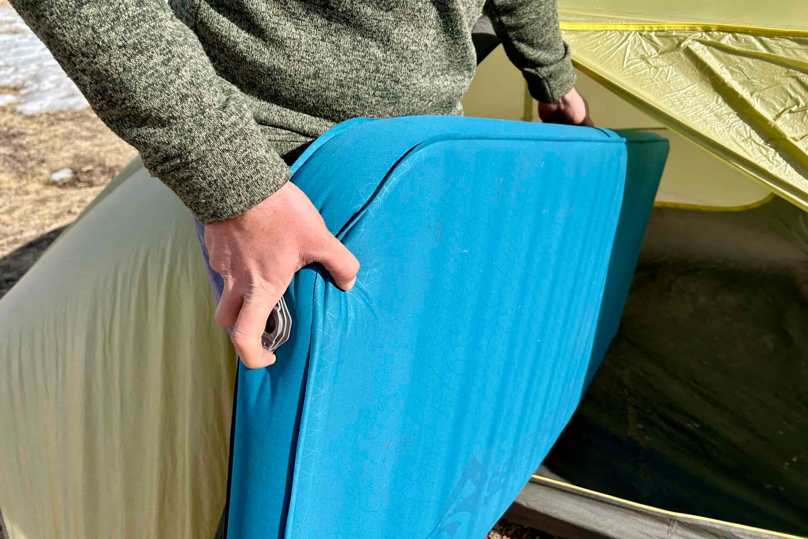 Close-up image of a person putting a camping mattress into a tent.