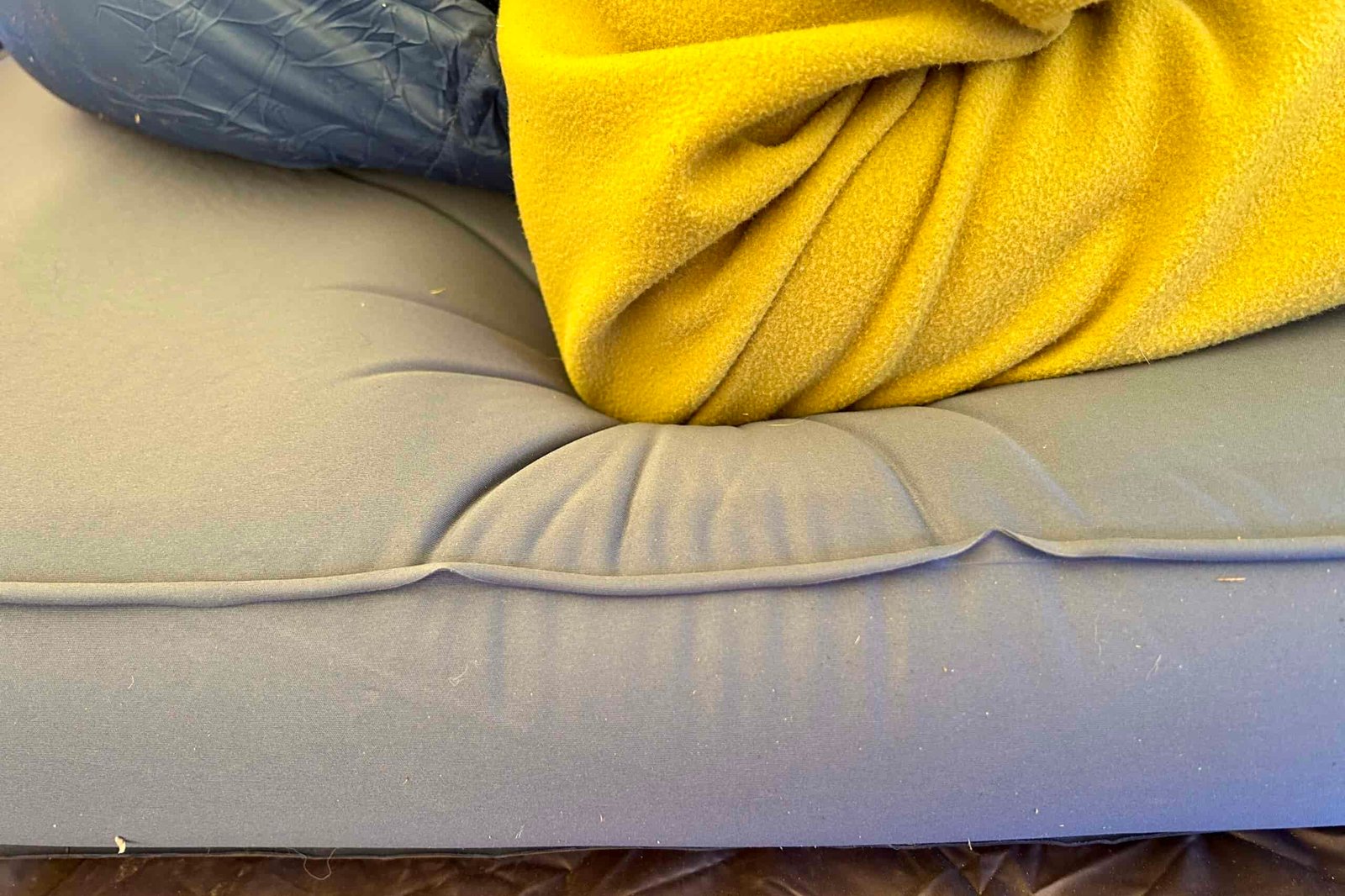Close-up image of someon'es elbow pushing into a camping mattress. There are slight folds in the fabric from the pressure.