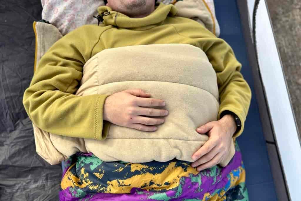 Close up image from above of a person laying in a sleeping bag with the edge folded down like a blanket, and their arms on top.