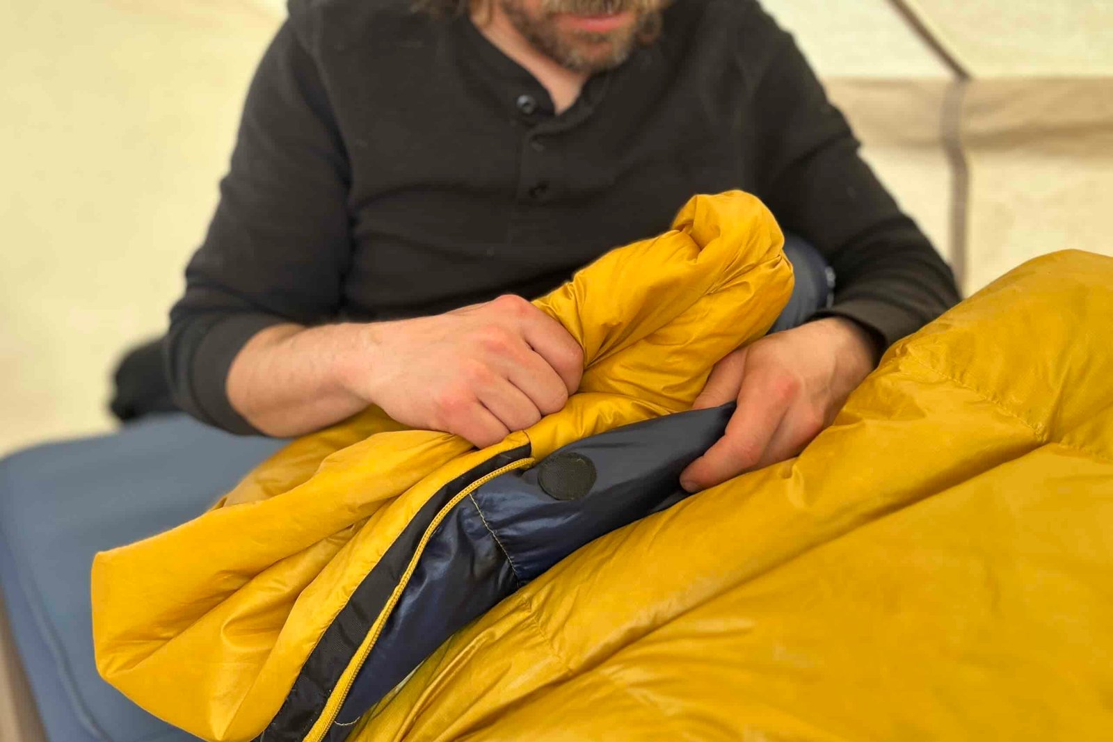 Close-up image of a person sitting up in a sleeping bag, clutching the fluffy draft tube and material on top.