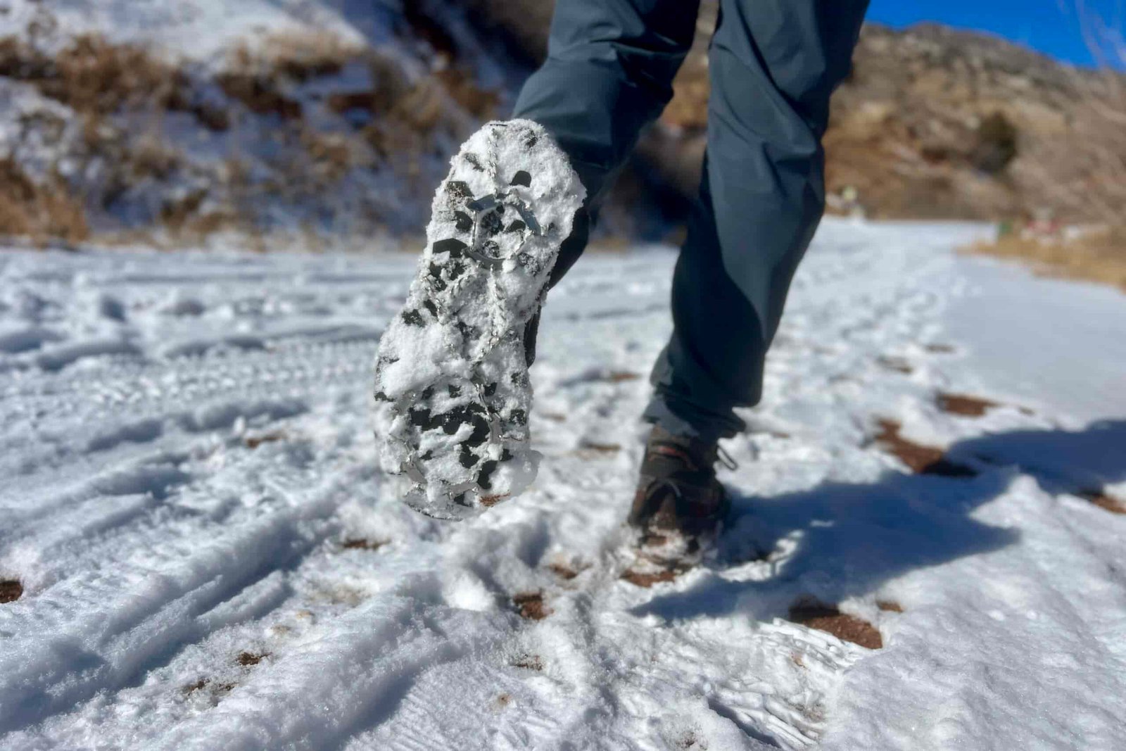 The under side of a hiker's foot while walking away with an ice cleat and snow on the bottom.