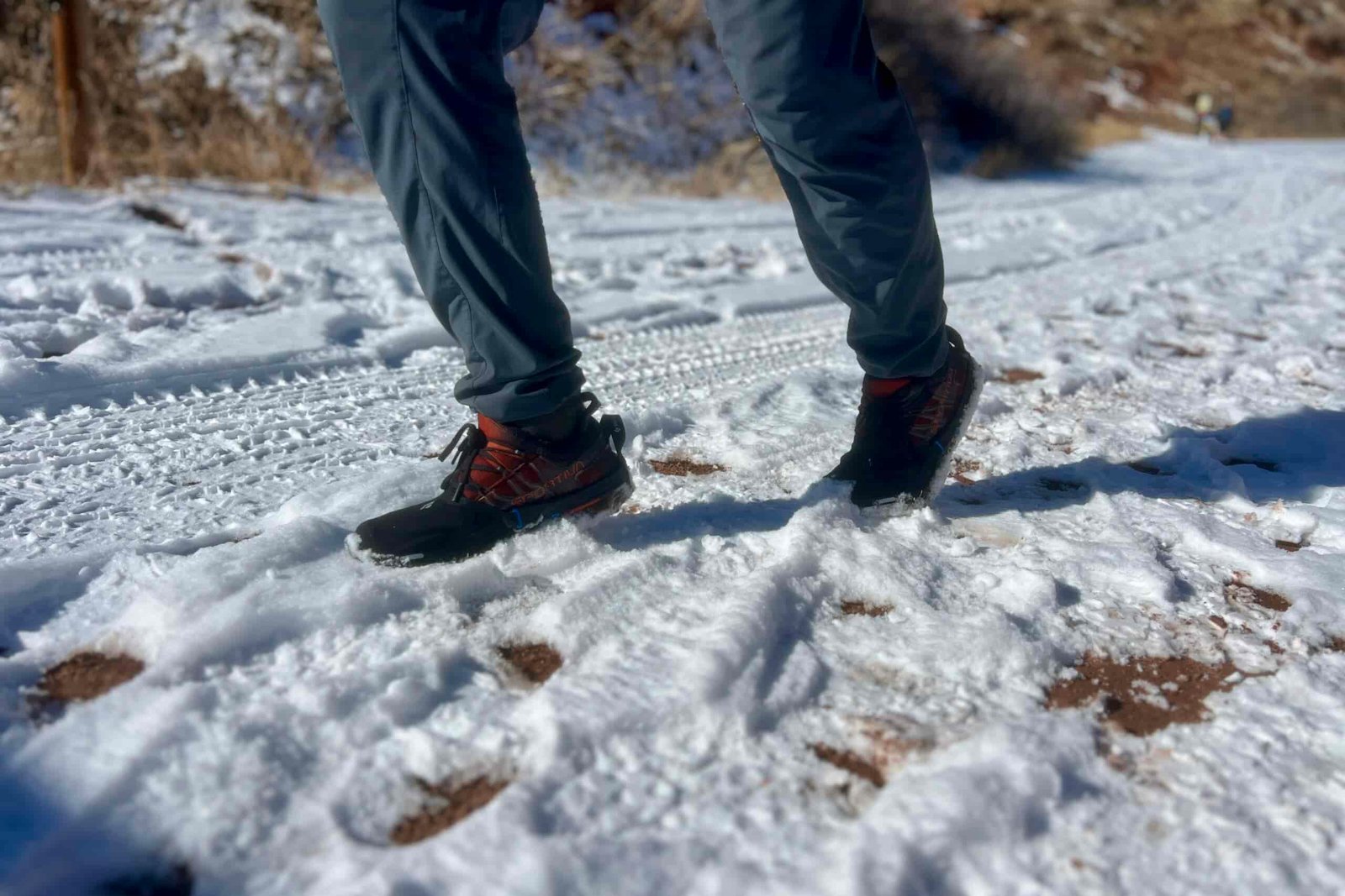 A hiker runs on snowy ground with a pair of ice cleats on a desert background.
