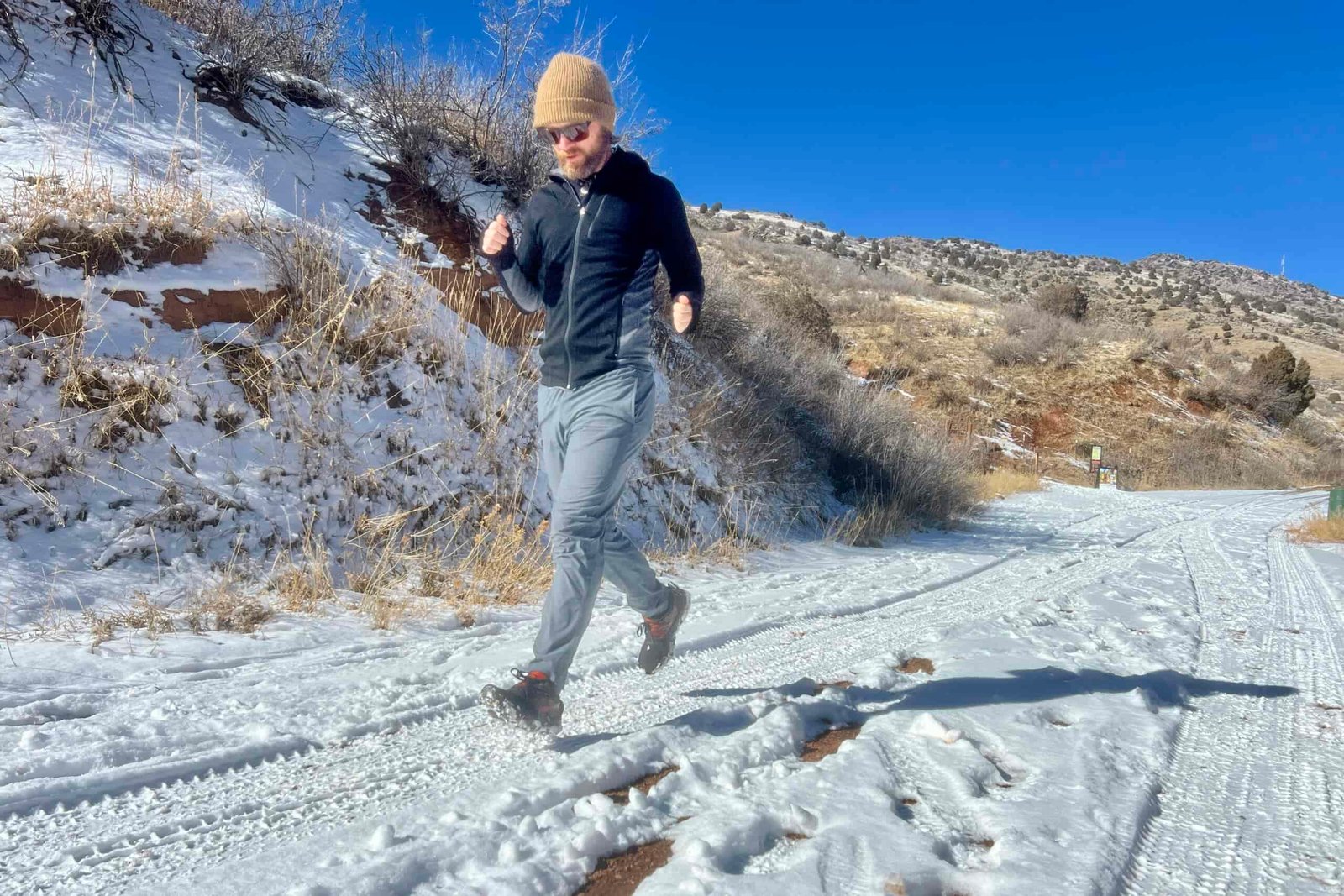 A hiker runs on snowy ground with a pair of ice cleats on a desert background.