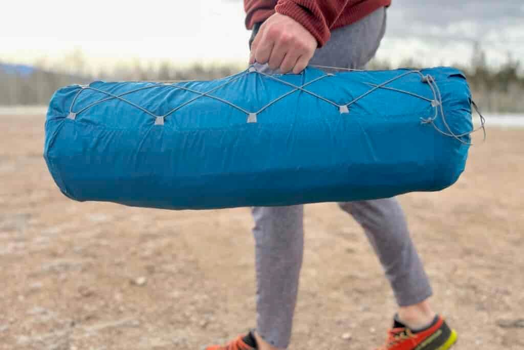Close-up image of a person walking with a packaged camping mattress at their side.