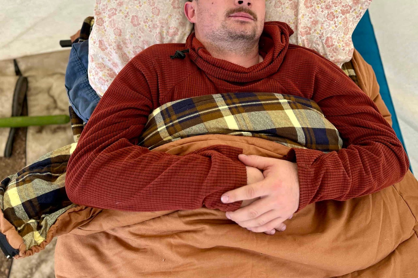 Close-up shot of a man in a sleeping bag with his arms resting on his chest.