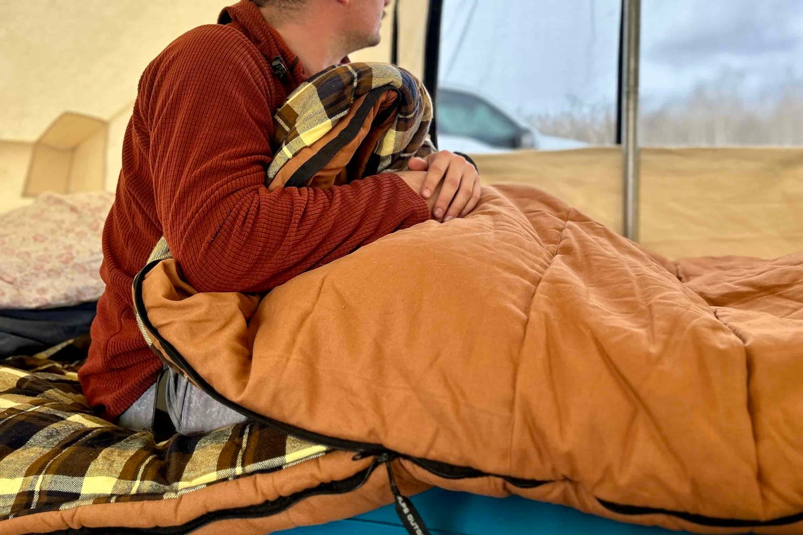 A man sits up in a sleeping bag on a sleeping pad with the material pulled around his waist.