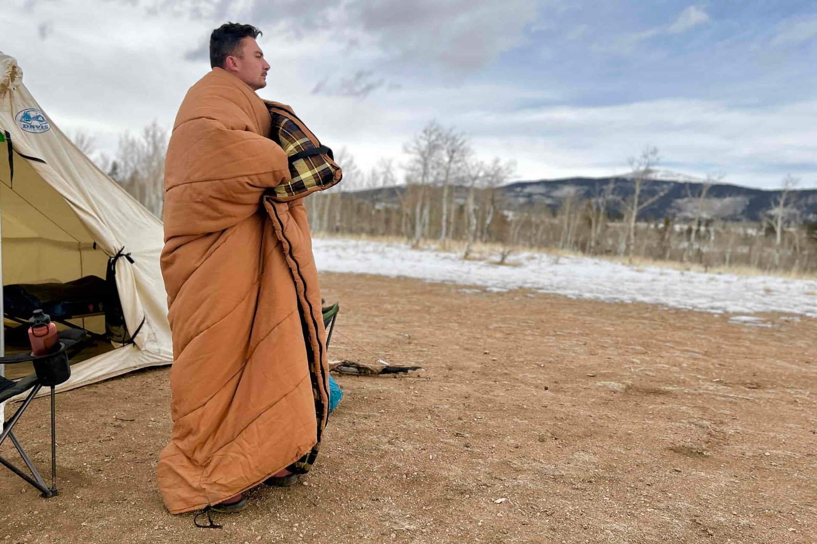 A man stands outside wrapped up in a sleeping bag.