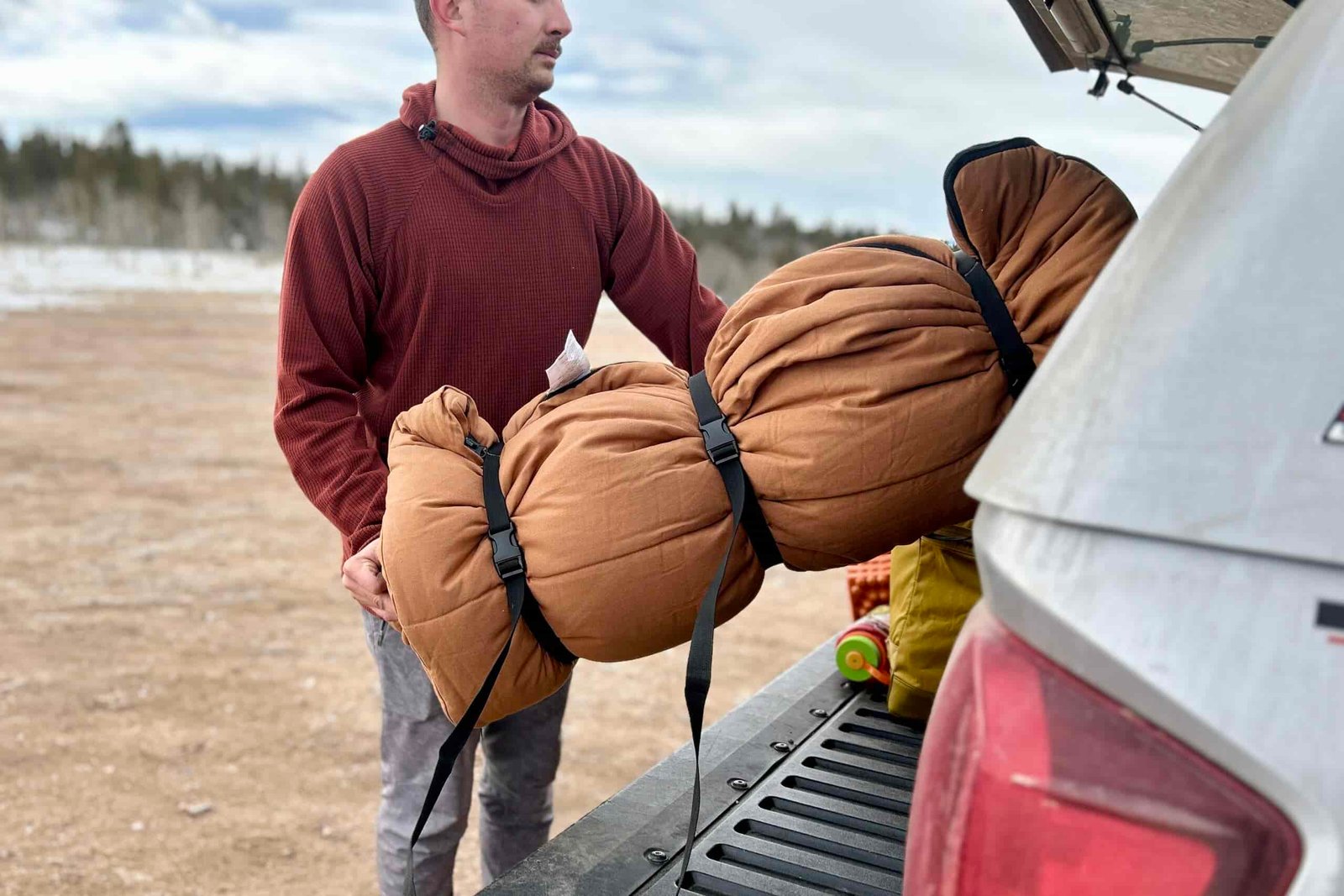 A man loads a very large sleeping bag, rolled up into a long tube shape, into the back of a truck.
