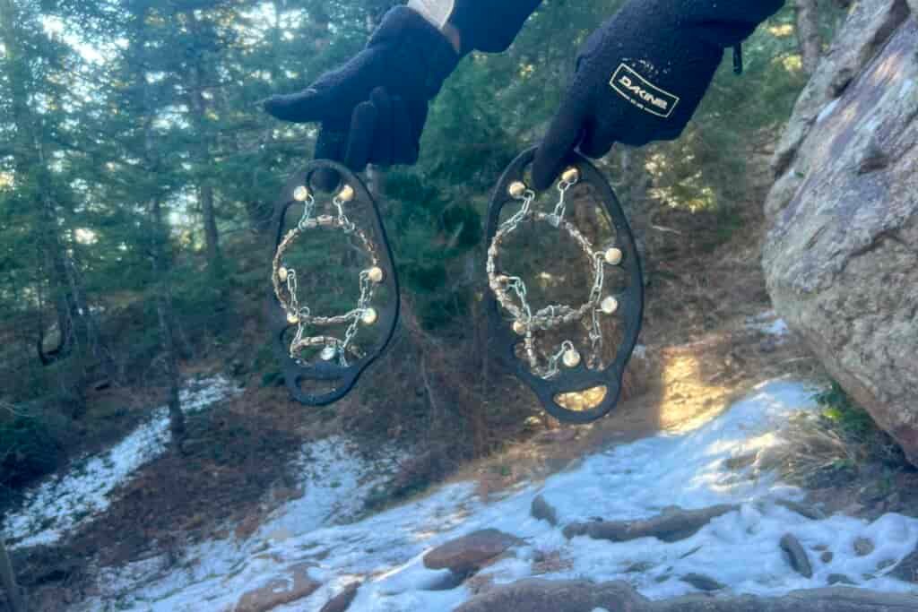 A hand holds a pair of ice cleats against a forest background.