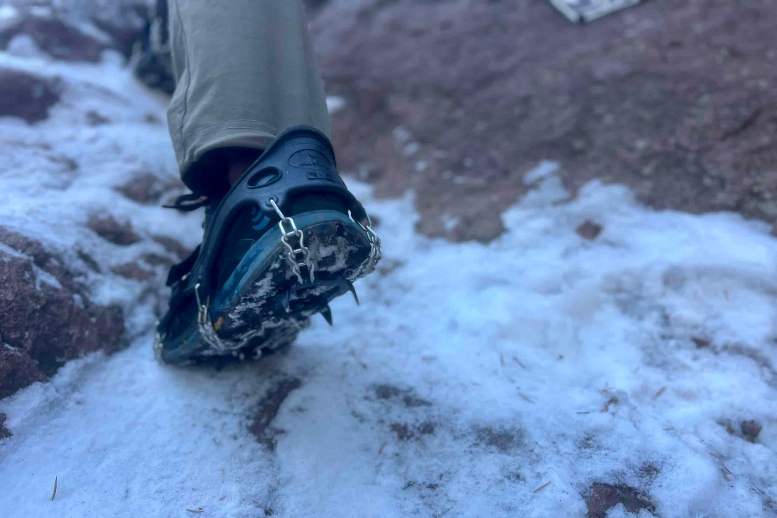 A foot scales an icy rock face with a pair of ice spikes.