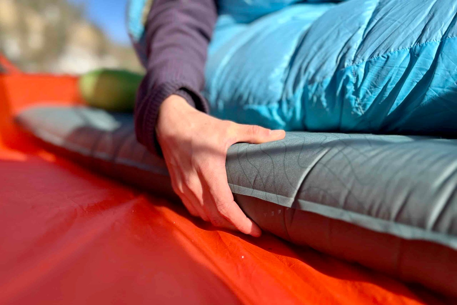 Close-up image of a person's hand holding onto the side of a sleeping pad.