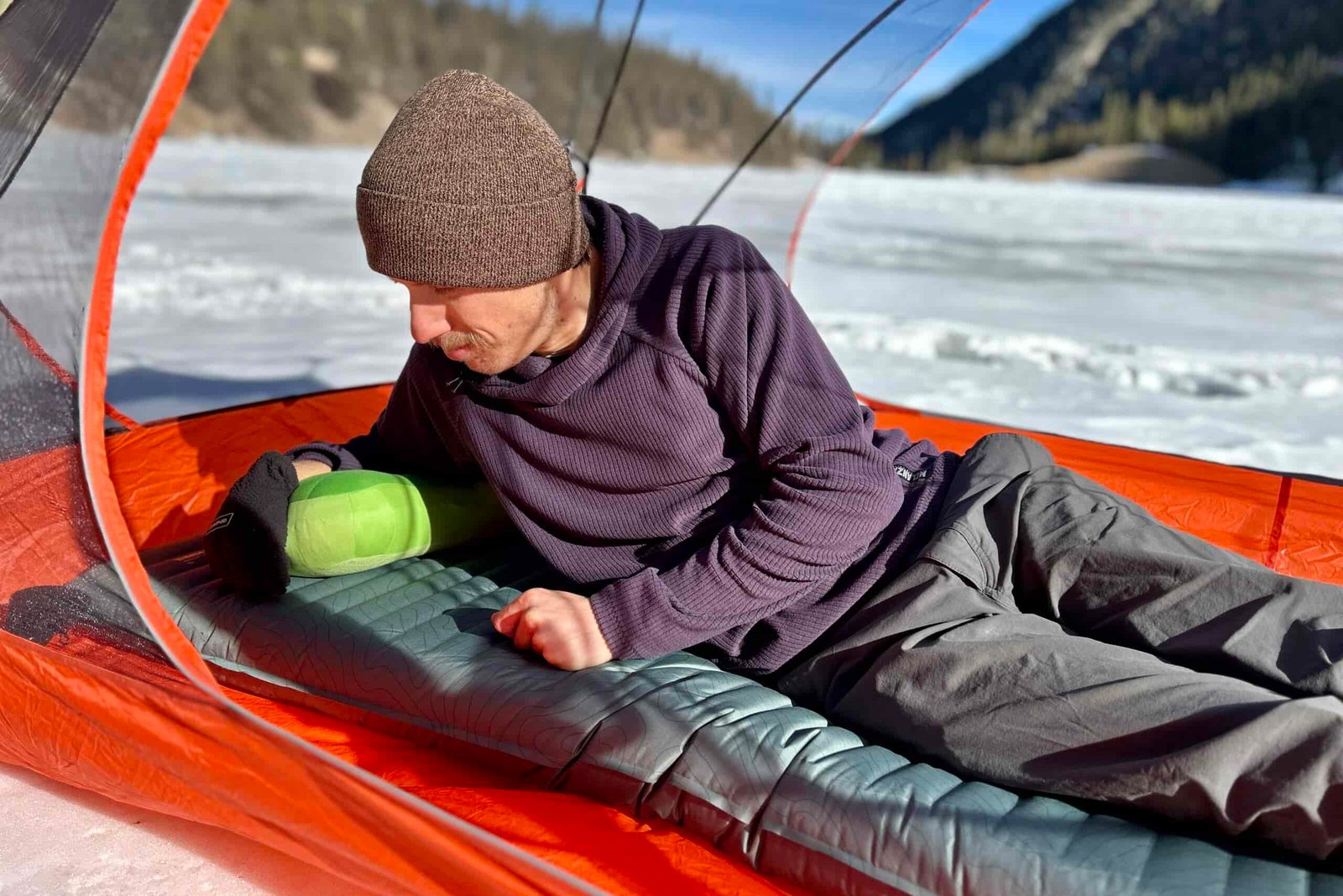 A man rests on a sleeping pad in a tent in a wintry setting.