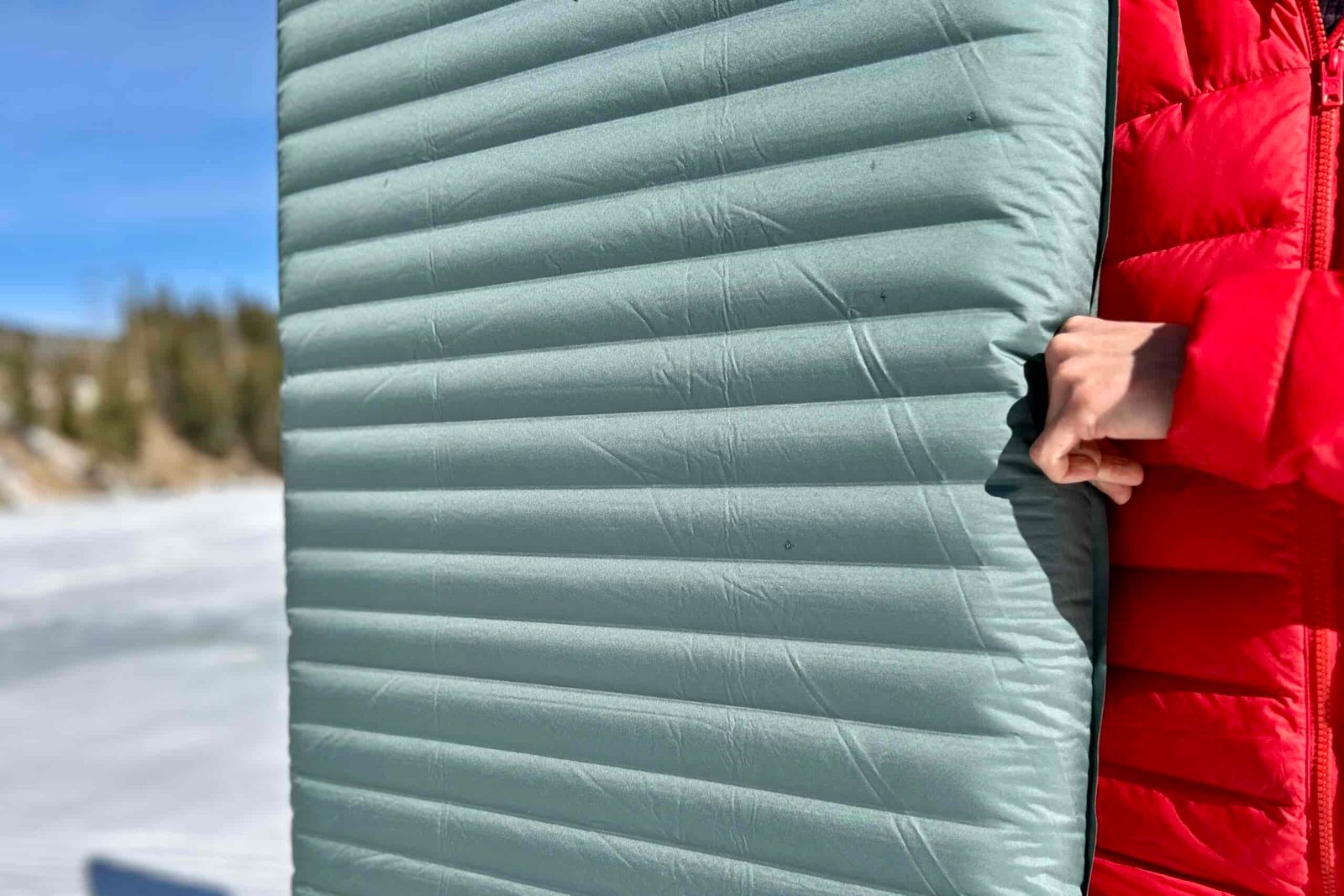 Close-up image of a person holding a sleeping bag with the smooth texture and narrow baffles visible.