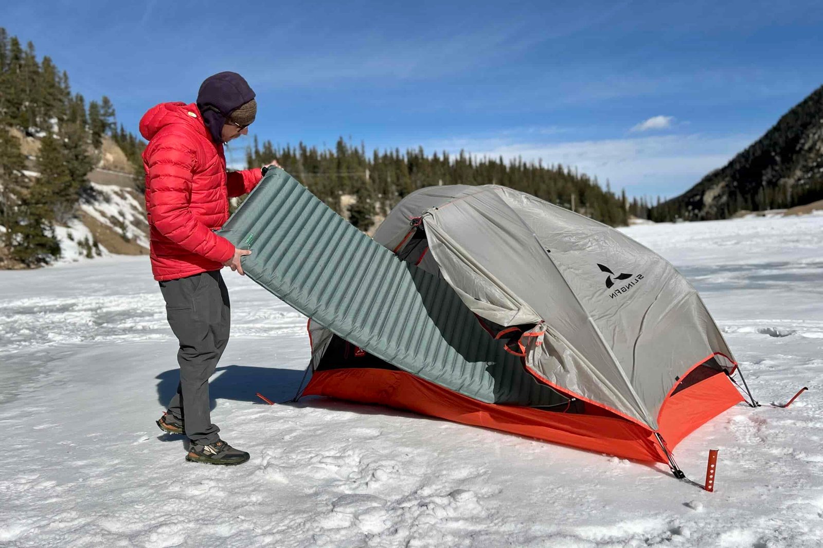 A man slides a camping mattress into a tent in a wintry setting.