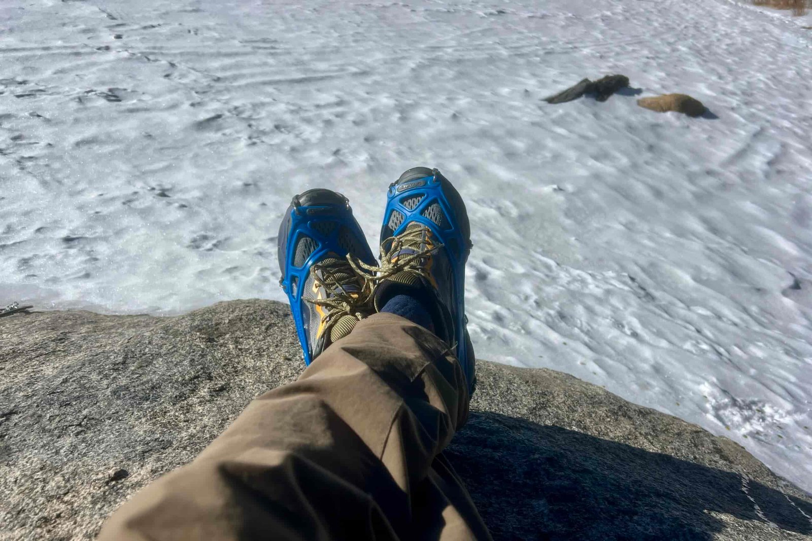 Two feet crossed while wearing ice cleats against a snowy background
