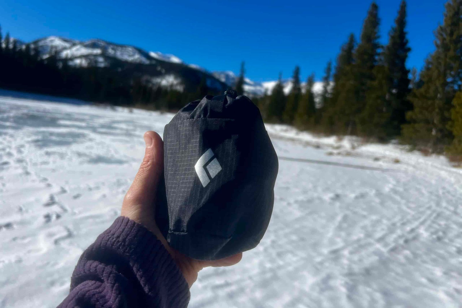 A hand holds out a black diamond stuff sack against a sunny winter background.