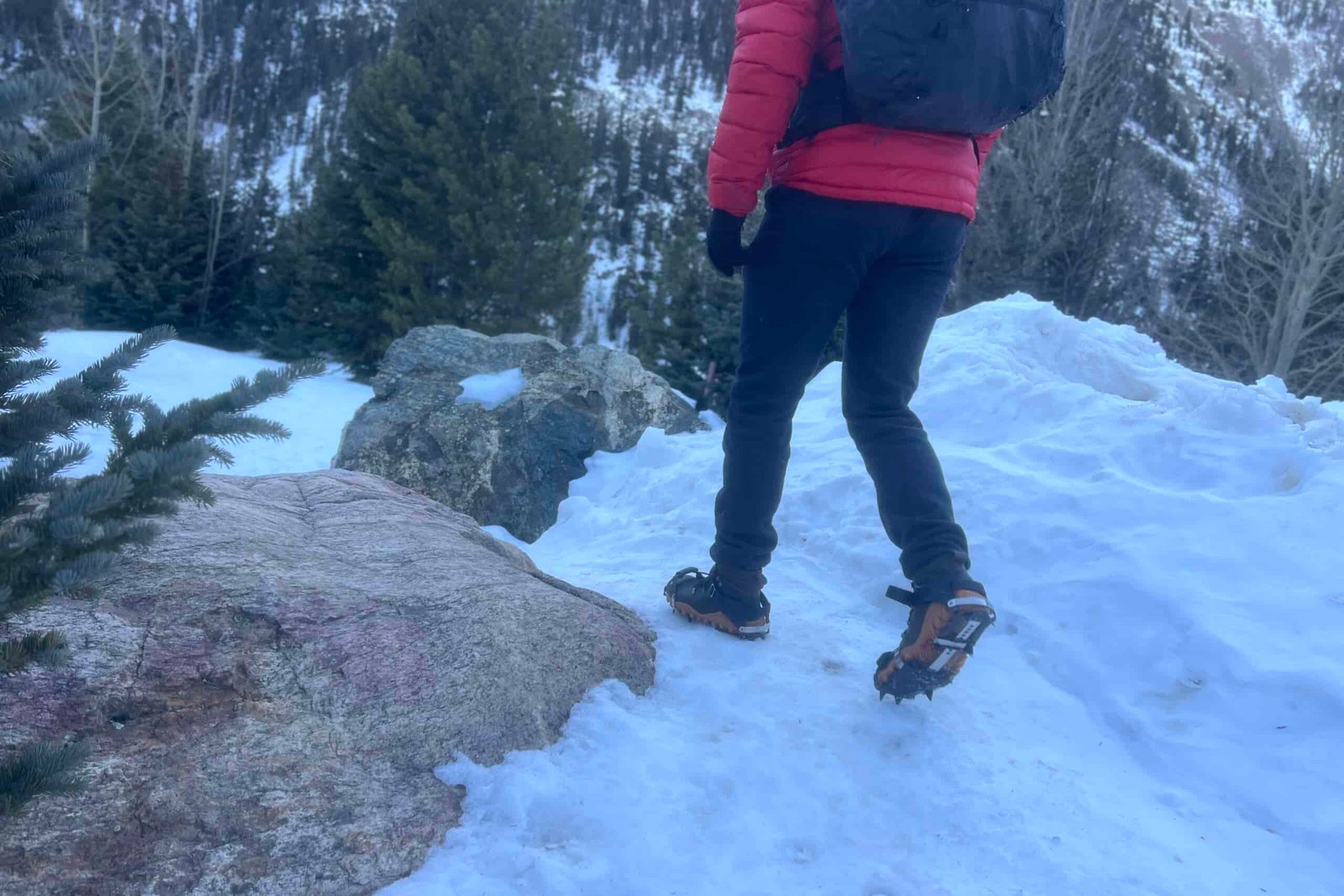 a hiker walks towards the camera on a snowy trail with a pair of aggressive trail crampons.