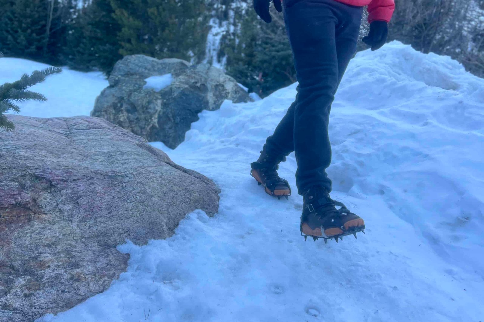 a hiker walks towards the camera on a snowy trail with a pair of aggressive trail crampons.