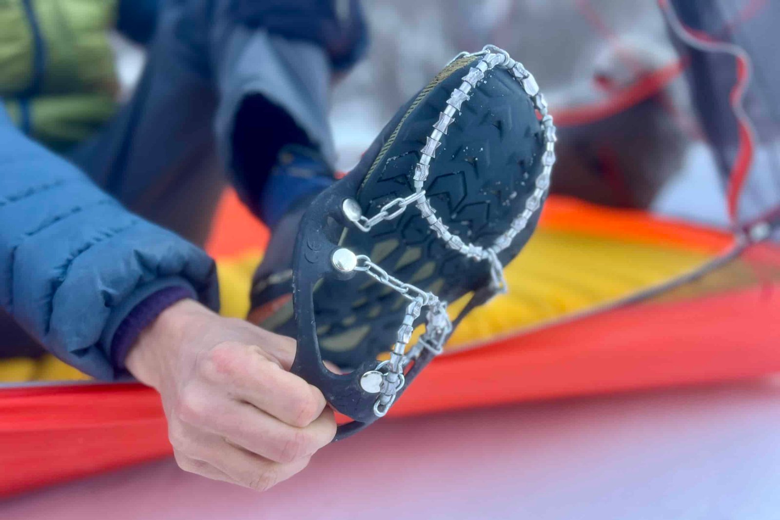 A hiker sits in a tent and pull off a pair of ice cleats from his feet.